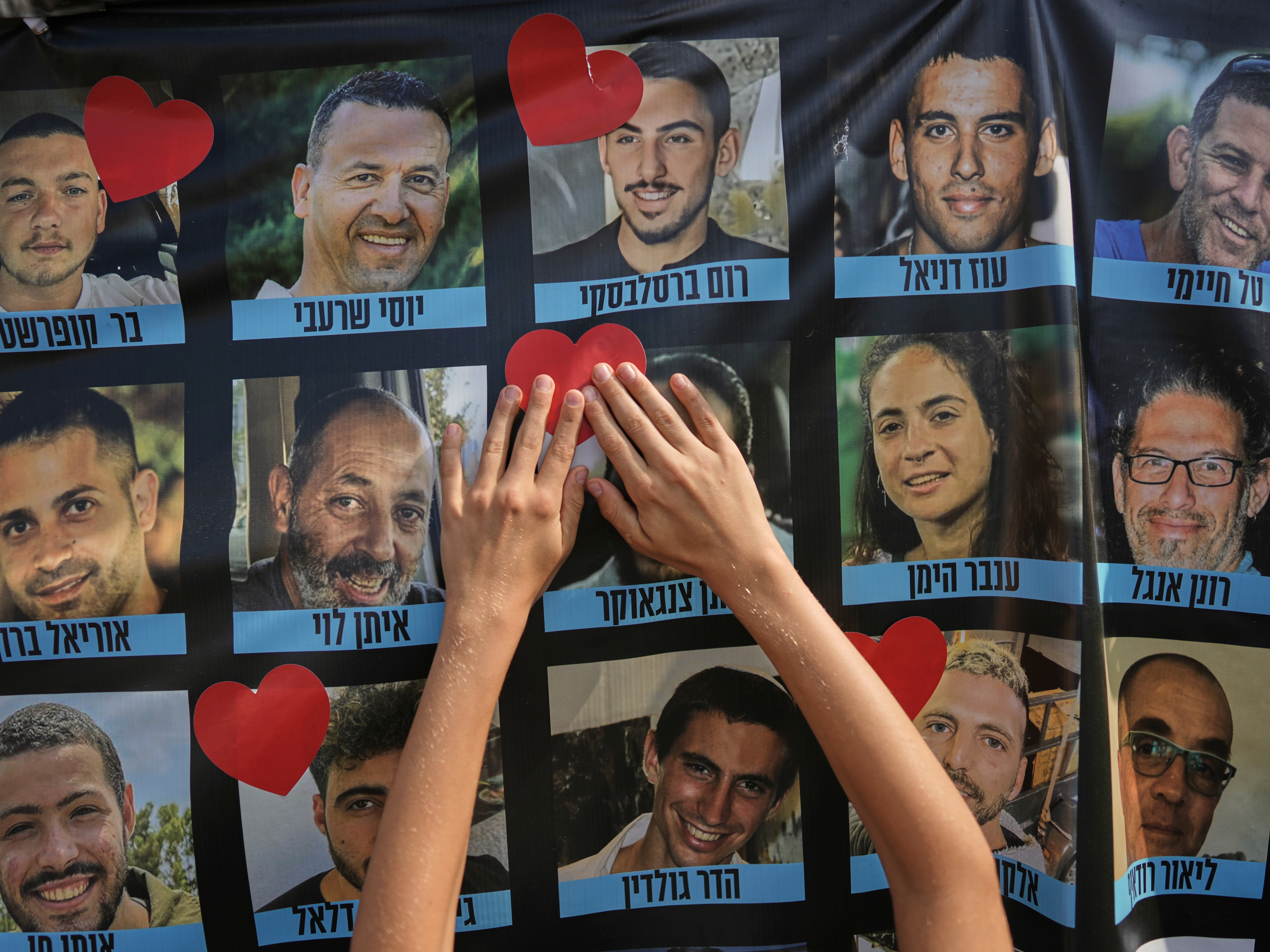 caption: A person pastes a heart-shaped sticker on a banner with pictures of Israeli hostages during a a gathering at a plaza known as hostages square in Tel Aviv, Israel, Monday.