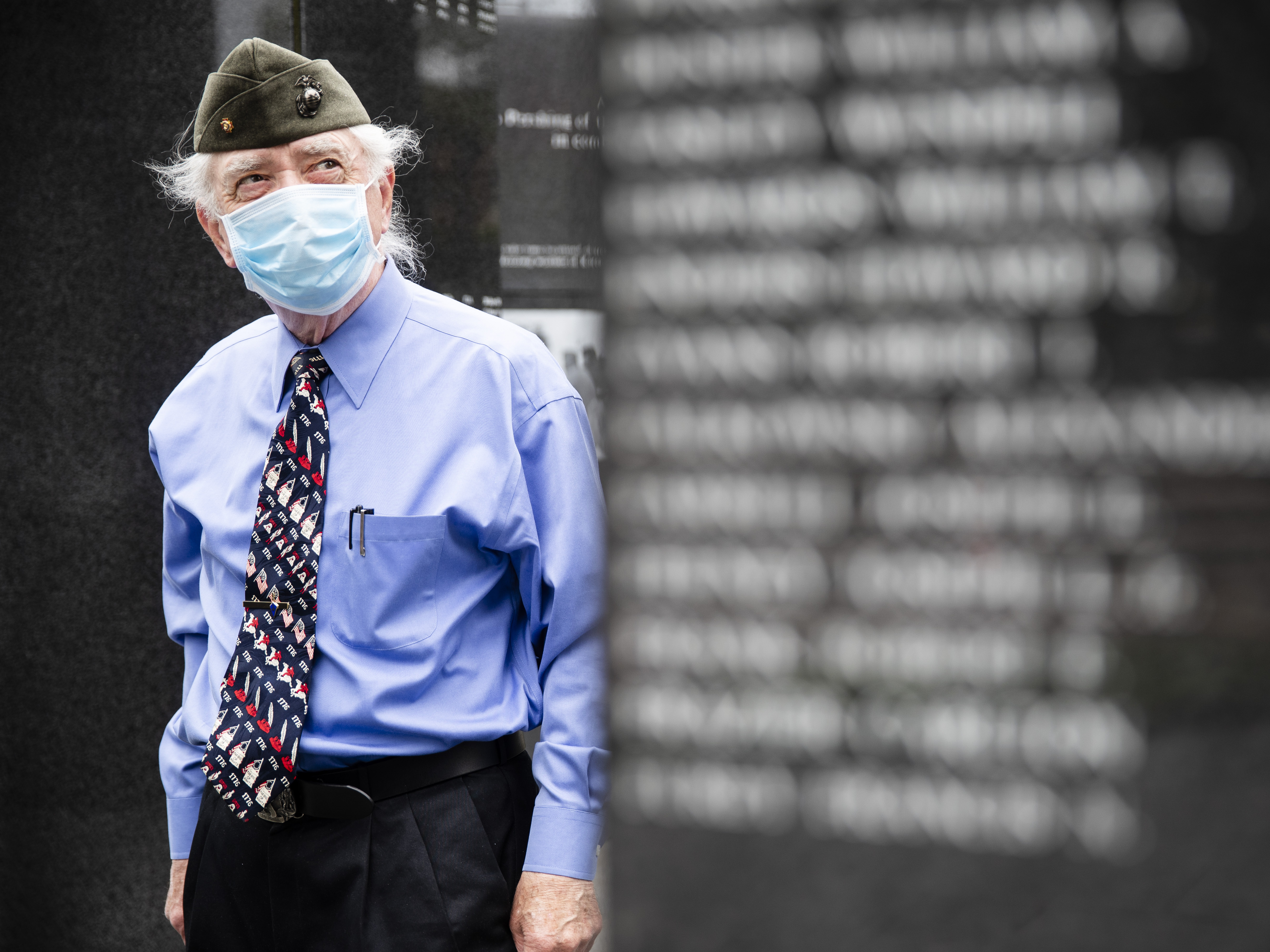 caption: A U.S. Marine Corps veteran pays his respects at the Korean War Memorial behind a face mask in Philadelphia.