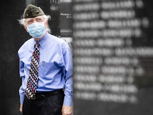caption: A U.S. Marine Corps veteran pays his respects at the Korean War Memorial behind a face mask in Philadelphia.