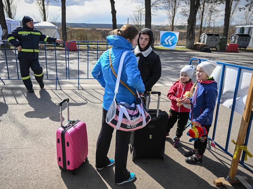 caption: A Ukrainian refugee speaks with a local interpreter as she and her two children arrive at the Siret border crossing between Romania and Ukraine on April 18.