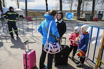 caption: A Ukrainian refugee speaks with a local interpreter as she and her two children arrive at the Siret border crossing between Romania and Ukraine on April 18.