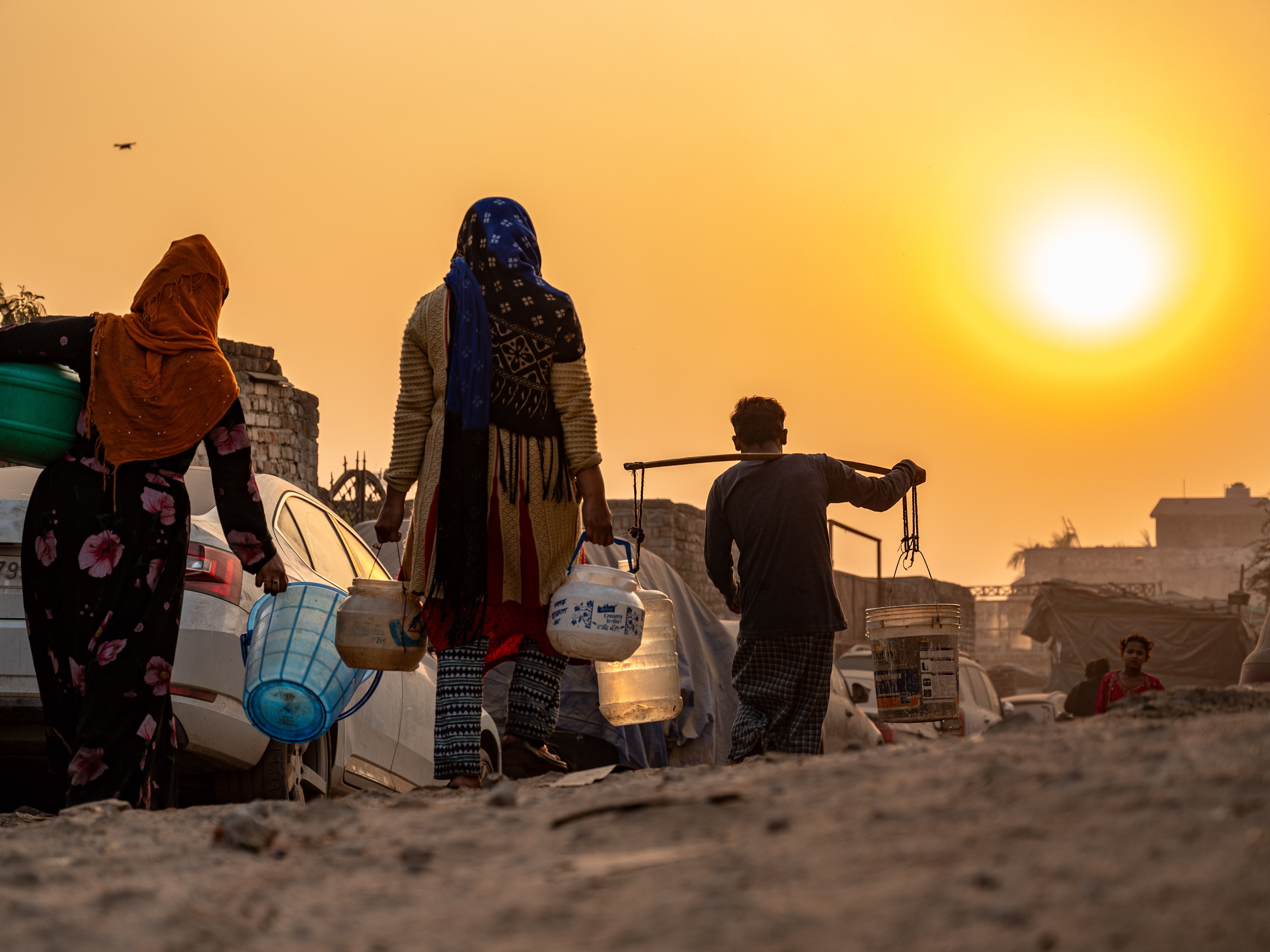 caption: A Rohingya refugee woman walks home, carrying a container of drinking water fetched from a distribution point in Madanpur Khadar Rohingya refugee camp, in New Delhi, India.