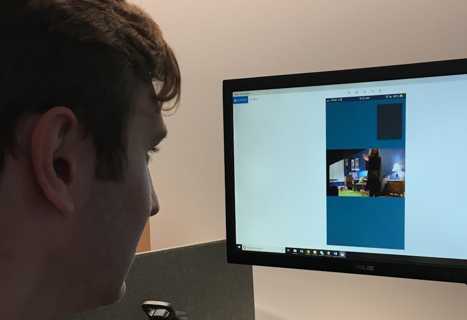 caption: Cameron Bulanda watches Joshua McNichols' Seattle living room from the offices of Infosec in Chicago. He hacked his Alexa account through a phishing attempt (with the reporter's permission).