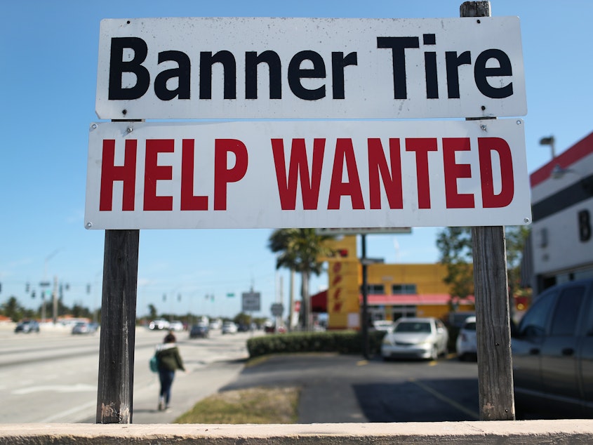 caption: A "Help Wanted" sign is posted in front of a business on Feb. 4 in Miami. Although millions are unemployed, some businesses that require being on-site are struggling to find workers.