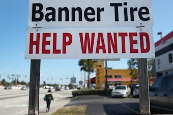 caption: A "Help Wanted" sign is posted in front of a business on Feb. 4 in Miami. Although millions are unemployed, some businesses that require being on-site are struggling to find workers.