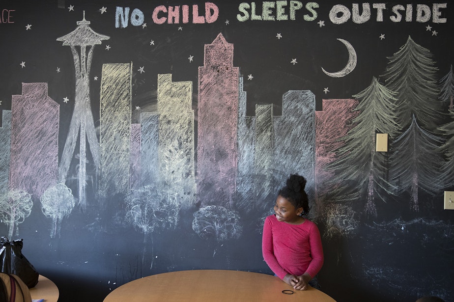 caption: Mariah Hicks, 7, stands in front of a chalk drawing depicting downtown Seattle in a common area at Mary's Place, a homeless shelter.