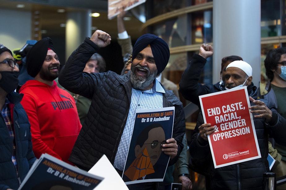 caption: Hira Singh Bhullar, center, raises his fist in the air while leading a chant during a rally ahead of a Seattle city council vote on a measure sponsored by councilmember Kshama Sawant that would ban discrimination based on caste, on Tuesday, February 21, 2023, at Seattle City Hall. Seattle would be the first city in the nation to do so.