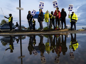 caption: Factory workers and UAW union members form a picket line outside the Ford Motor Co. Kentucky Truck Plant in the early morning hours on October 14, 2023 in Louisville, Kentucky.