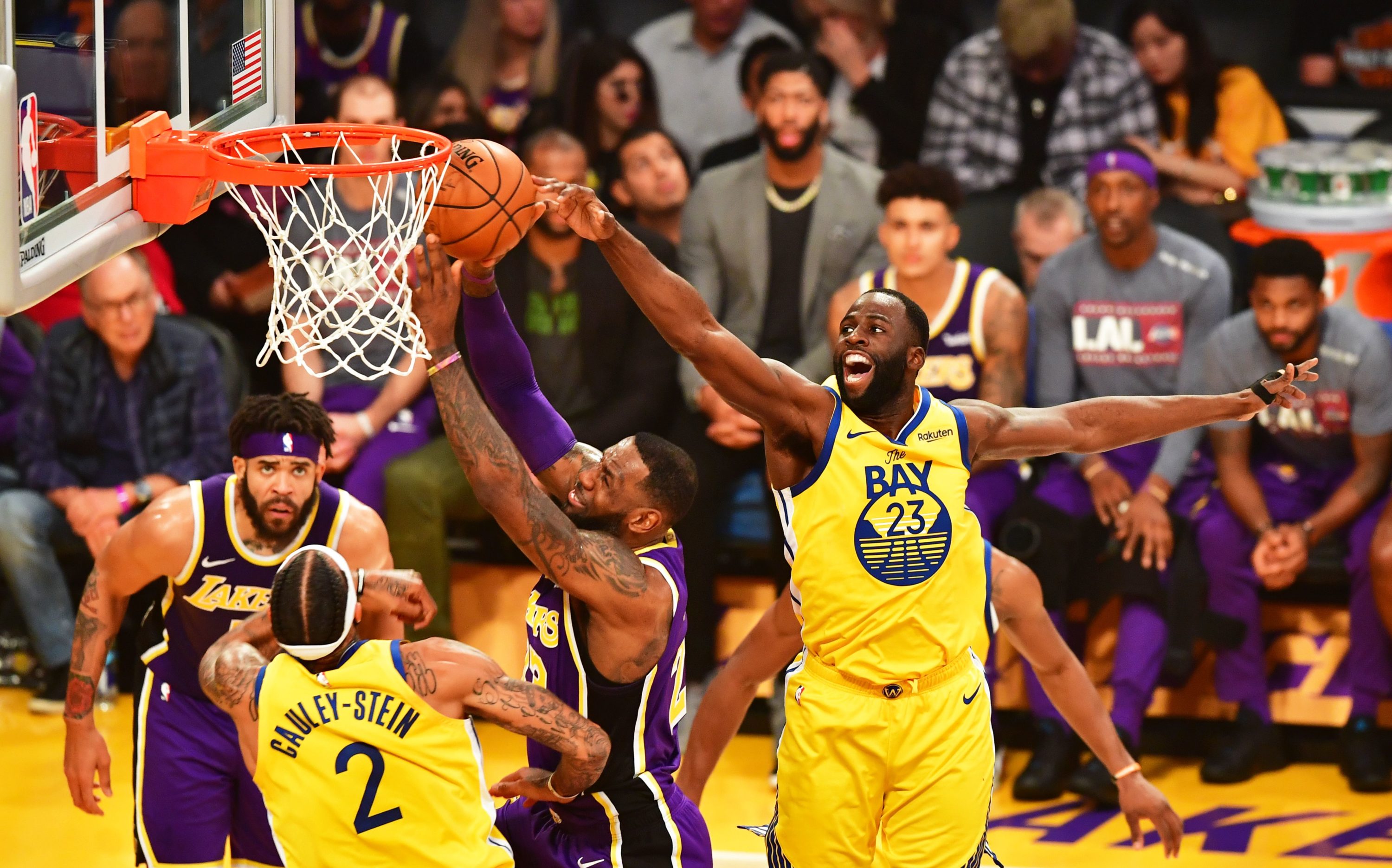 caption: LeBron James of the Los Angeles Lakers (C) goes to the hoop under pressure from Draymond Green (R) of the Golden State Warriors during their the regular season game at the Staples Center in Los Angeles on November 13, 2019. (FREDERIC J. BROWN/AFP via Getty Images)