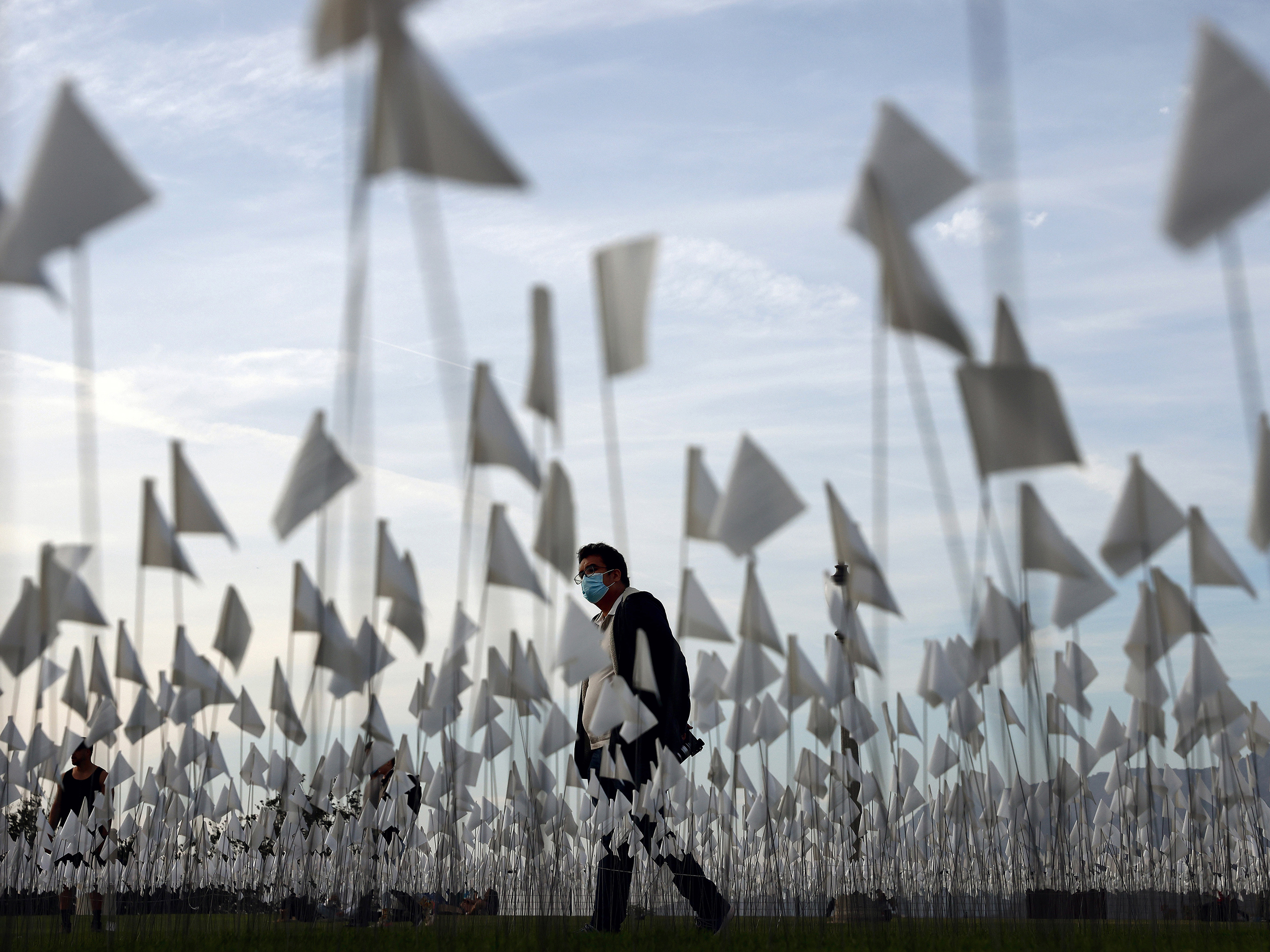 caption: A person wearing a face covering walks past a white flag memorial installation outside Griffith Observatory honoring the nearly 27,000 Los Angeles County residents who have died from COVID-19 on Nov. 18 in Los Angeles, Calif.