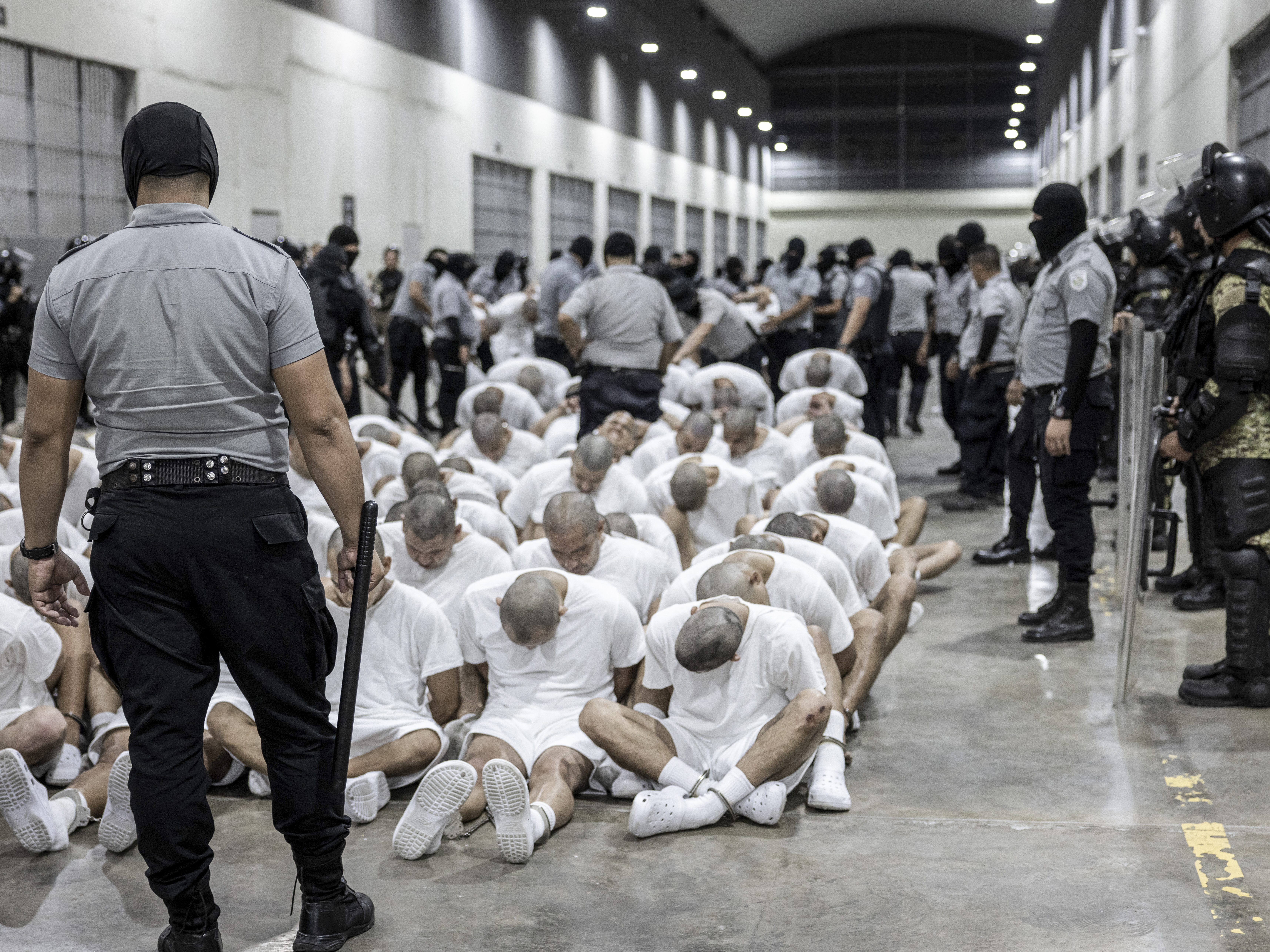 caption: In this photo provided by El Salvador's presidential press office, a prison guard transfers deportees from the U.S., alleged to be Venezuelan gang members, to the Terrorism Confinement Center in Tecoluca, El Salvador on Sunday.