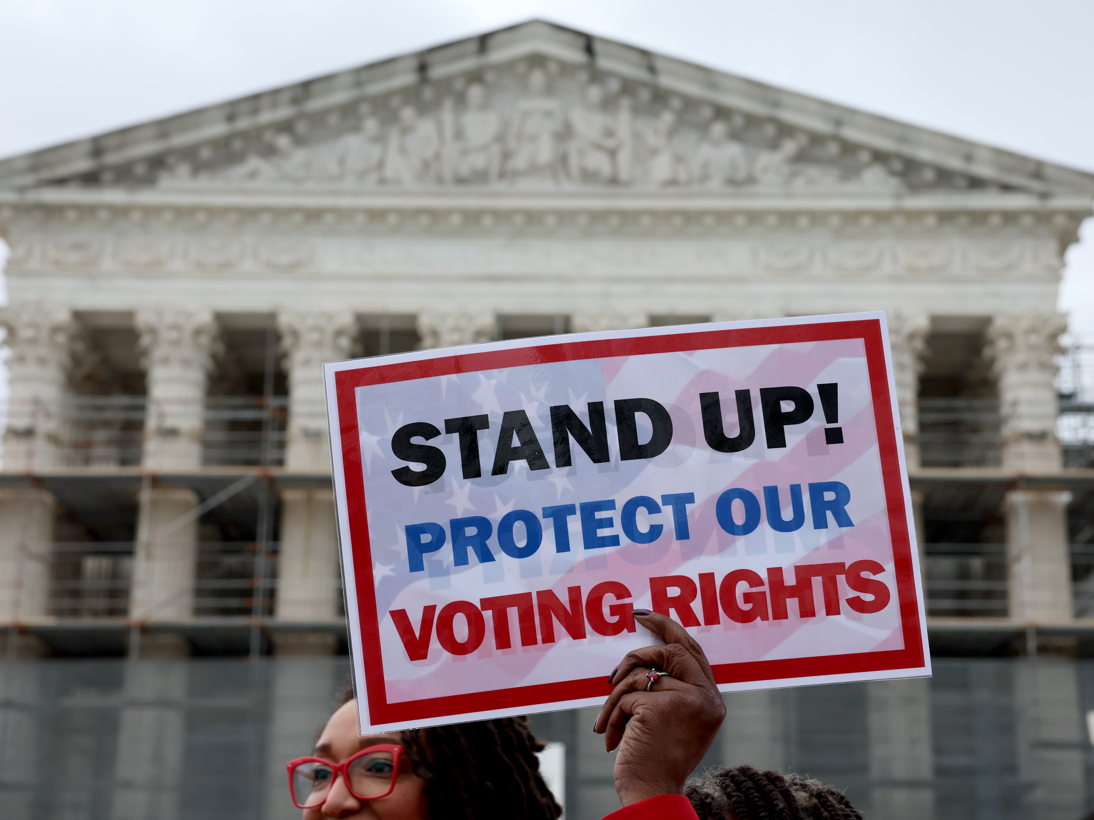 caption: A member of Delta Sigma Theta sorority holds up a sign saying "STAND UP! PROTECT OUR VOTING RIGHTS" outside the U.S. Supreme Court on Monday in Washington, D.C.