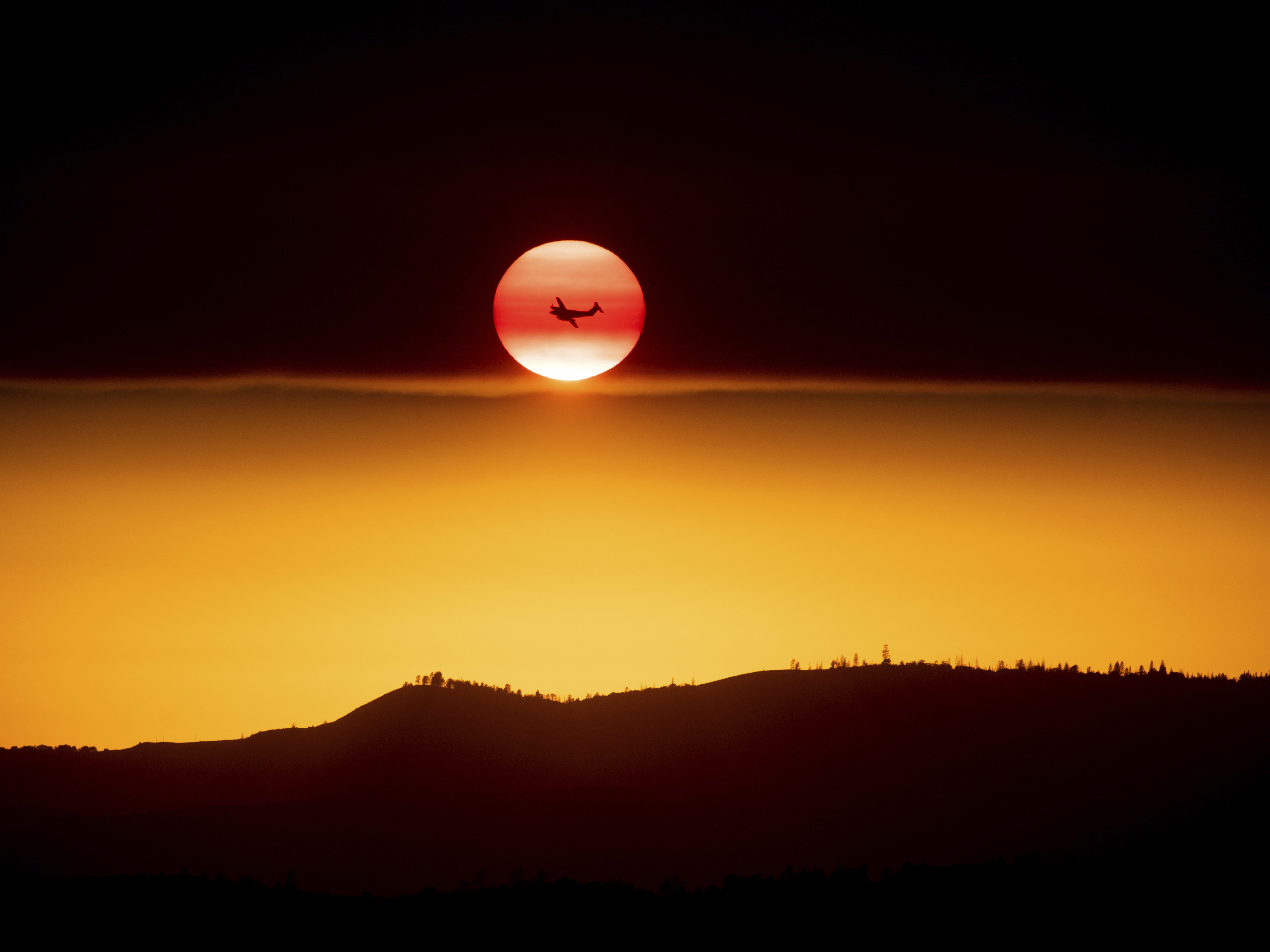caption: A plane battling the Ferguson Fire passes the setting sun in unincorporated Mariposa County Calif., near Yosemite National Park in July 2018.
