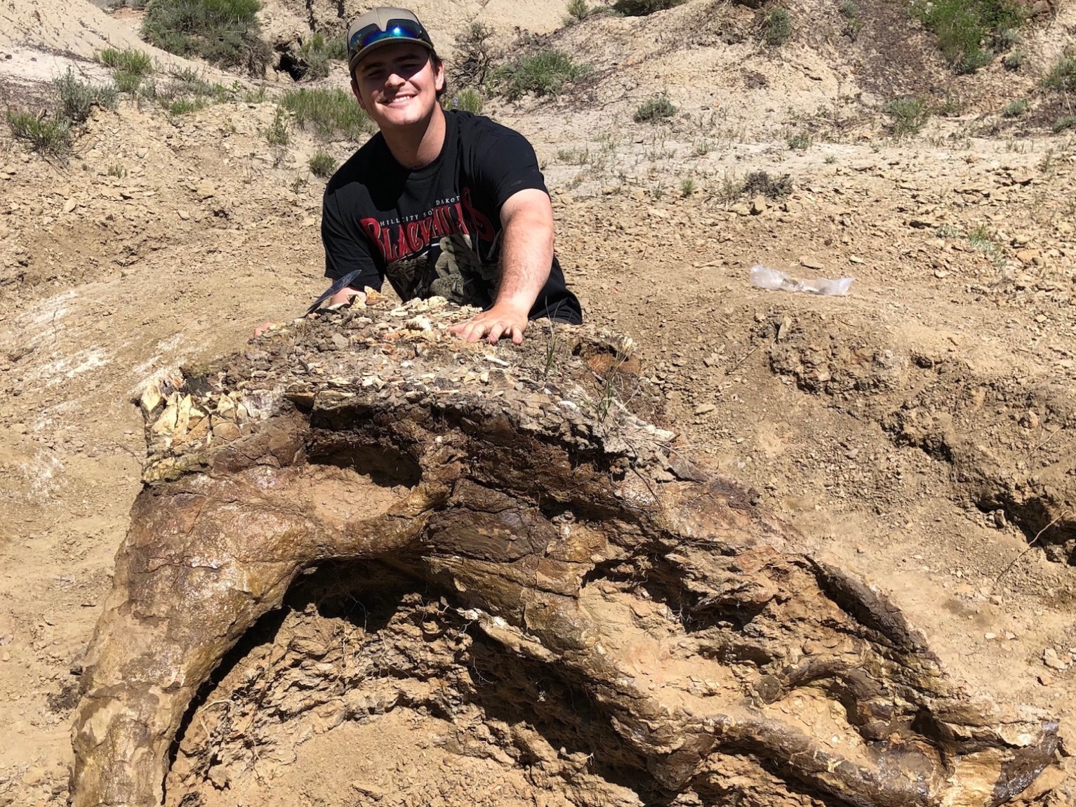 caption: Harrison Duran, 23, poses with Alice, the 65-million-year-old partial skull of a triceratops. The dinosaur-obsessed student helped find Alice on an expedition with the Fossil Excavators.
