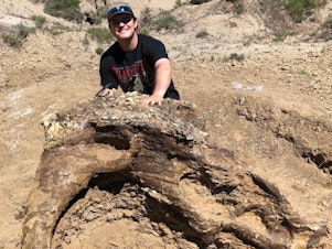 caption: Harrison Duran, 23, poses with Alice, the 65-million-year-old partial skull of a triceratops. The dinosaur-obsessed student helped find Alice on an expedition with the Fossil Excavators.