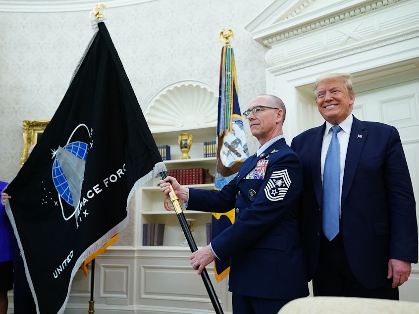 caption: President Trump presedisplays the U.S. Space Force flag in the Oval Office last May. The new command plans to move its headquarters from a temporary location in Colorado to Alabama in 2023.