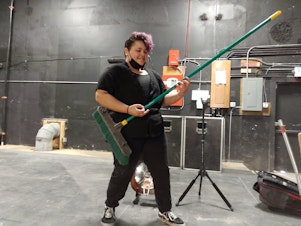 caption: Ari Whidbey playing a broom like a guitar onstage before a Rhapsody Project event at the Black and Tan Hall in Seattle, on March 5th, 2023.
