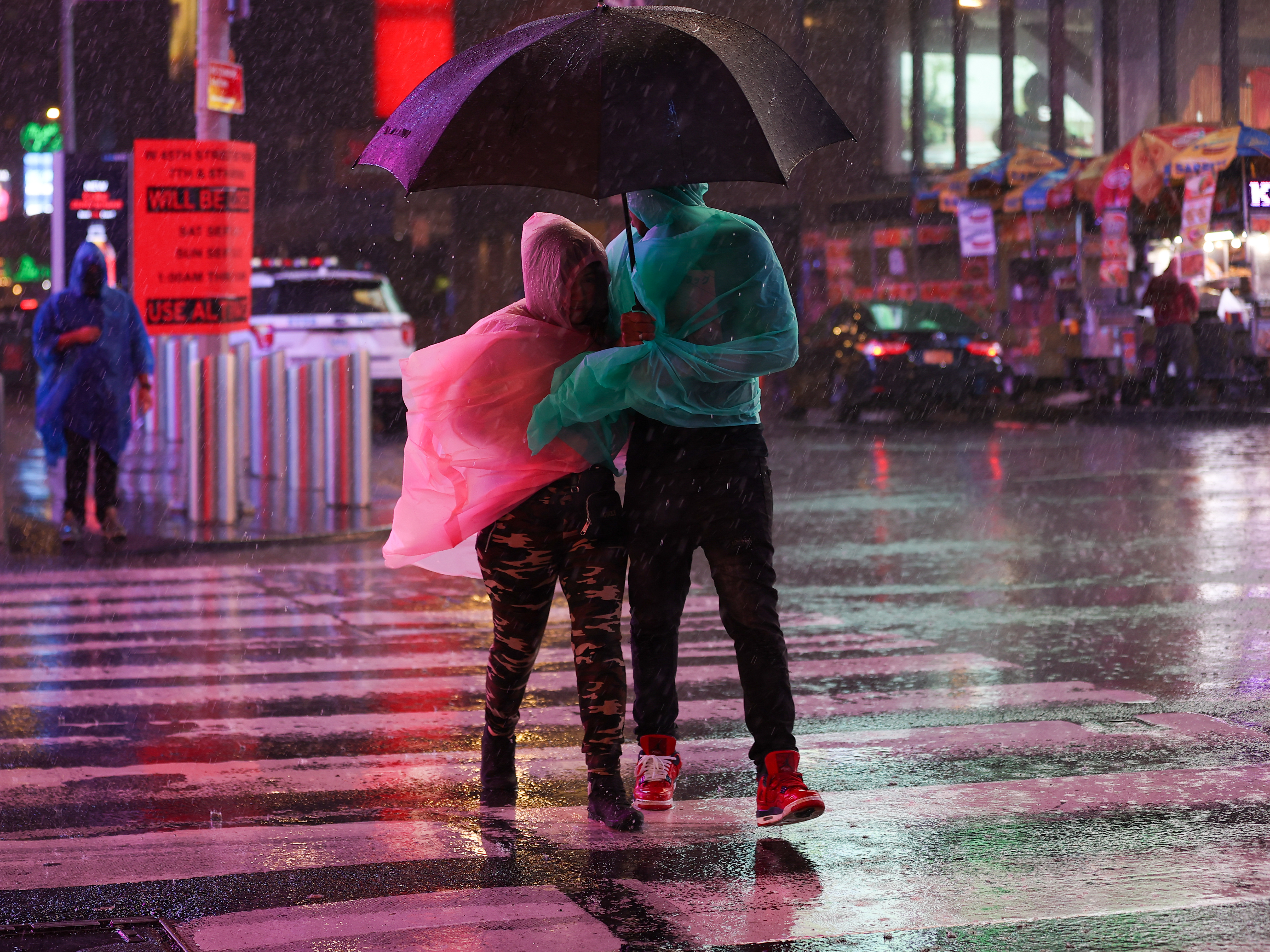 caption: People out in the street during heavy rain and storm at Times Square in New York City on September 1, 2021.