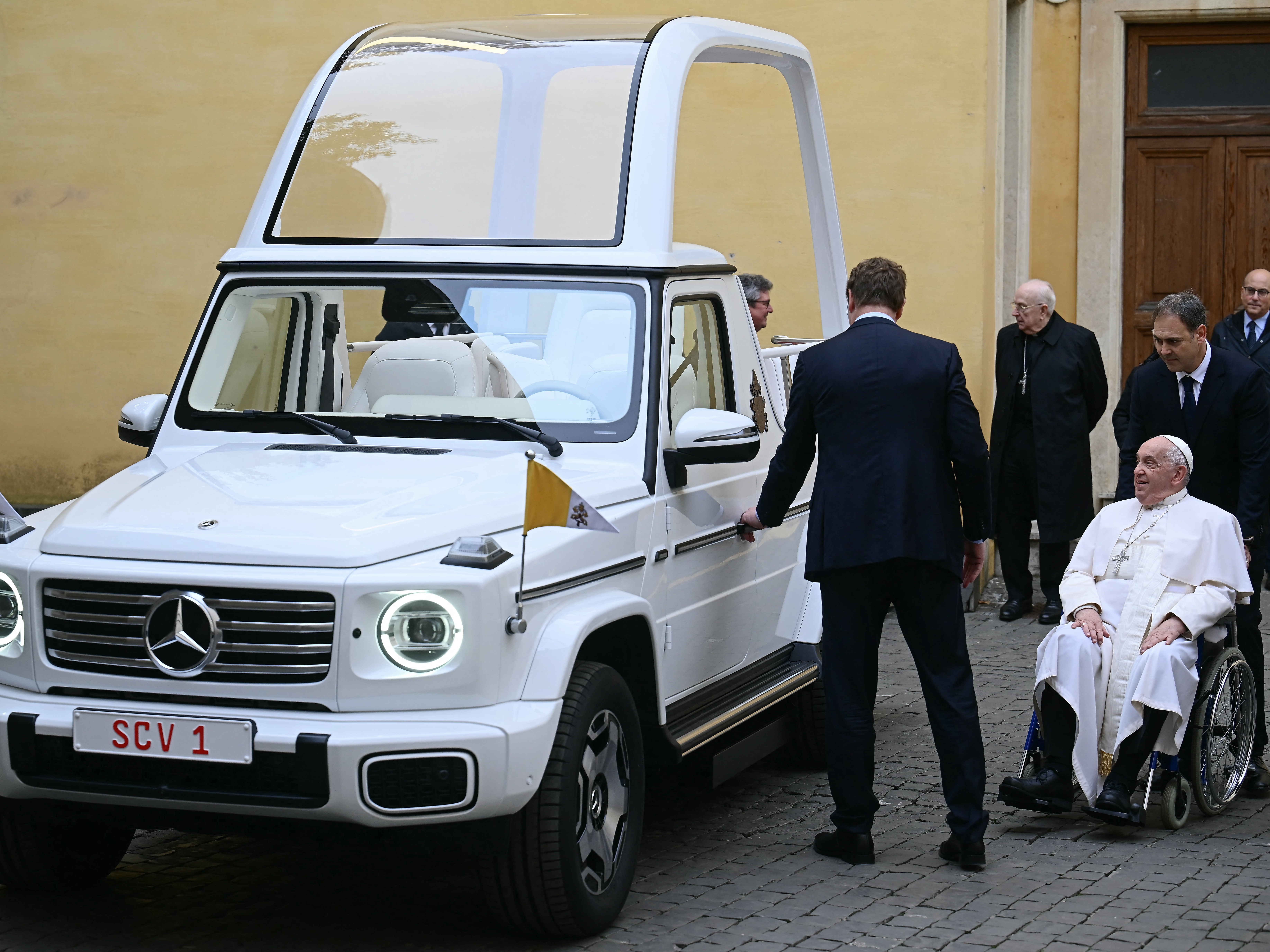 caption: Pope Francis (right) looks on as he's presented a new fully electric popemobile at the Vatican on Wednesday.