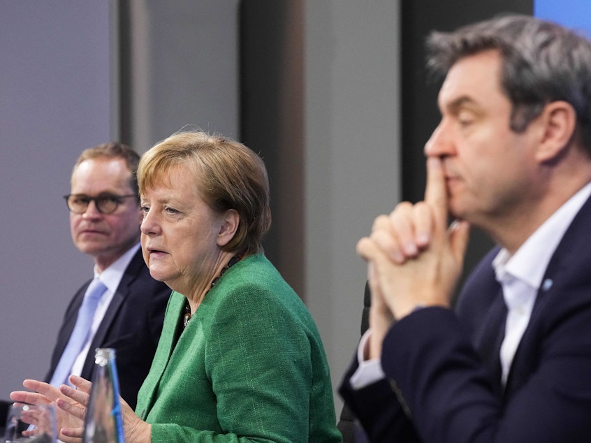 caption: German Chancellor Angela Merkel, with Bavaria's State Premier Markus Soeder (right) and Berlin's Mayor Michael Mueller, participate in a news conference following talks via video conference with Germany's state premiers on the extension of the current COVID-19 lockdown in Germany.