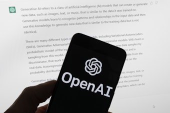 caption: The OpenAI logo is seen on a mobile phone in front of a computer screen displaying output from ChatGPT, Tuesday, March 21, 2023, in Boston.