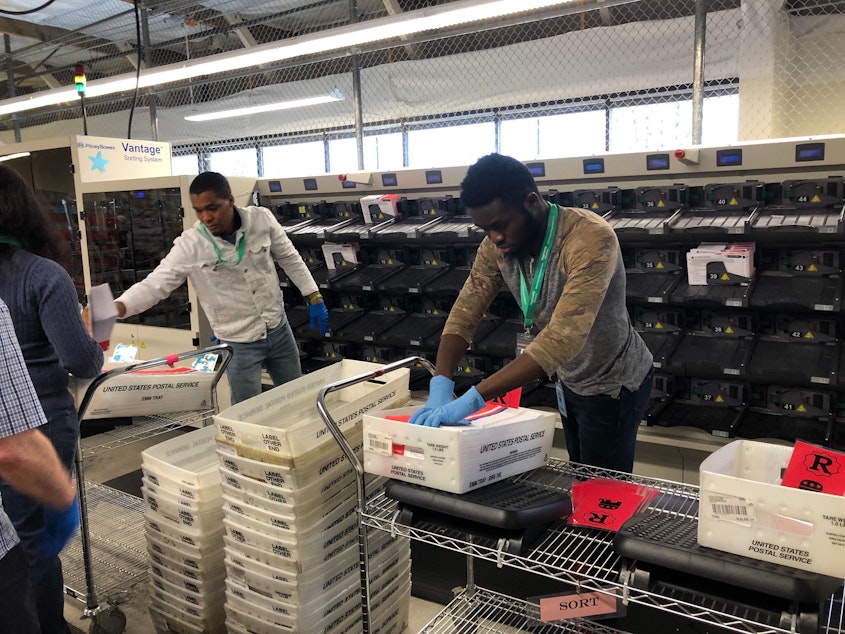 caption: Gloves are mandatory for King County elections staff like Dunia Wabenga, right.