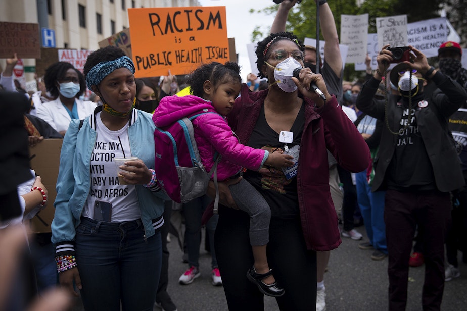 caption: Organizer Dr. Estell Williams, center, holds daughter Estella while speaking to a crowd of thousands who gathered in protest of police violence and to demand justice before marching from Harborview Medical Center to Seattle City Hall on Saturday, June 6, 2020, in Seattle. 