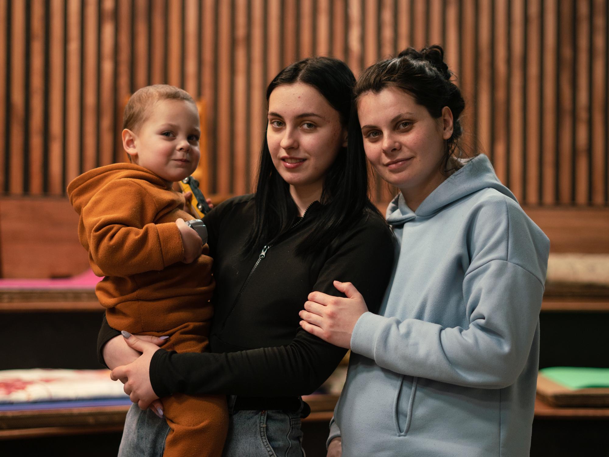 caption: Maksim, 2, is held by his aunt Beliakova (center) with her sister, his mother, Kuzhukhar.
