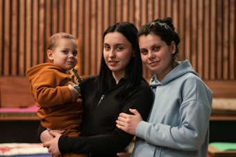 caption: Maksim, 2, is held by his aunt Beliakova (center) with her sister, his mother, Kuzhukhar.