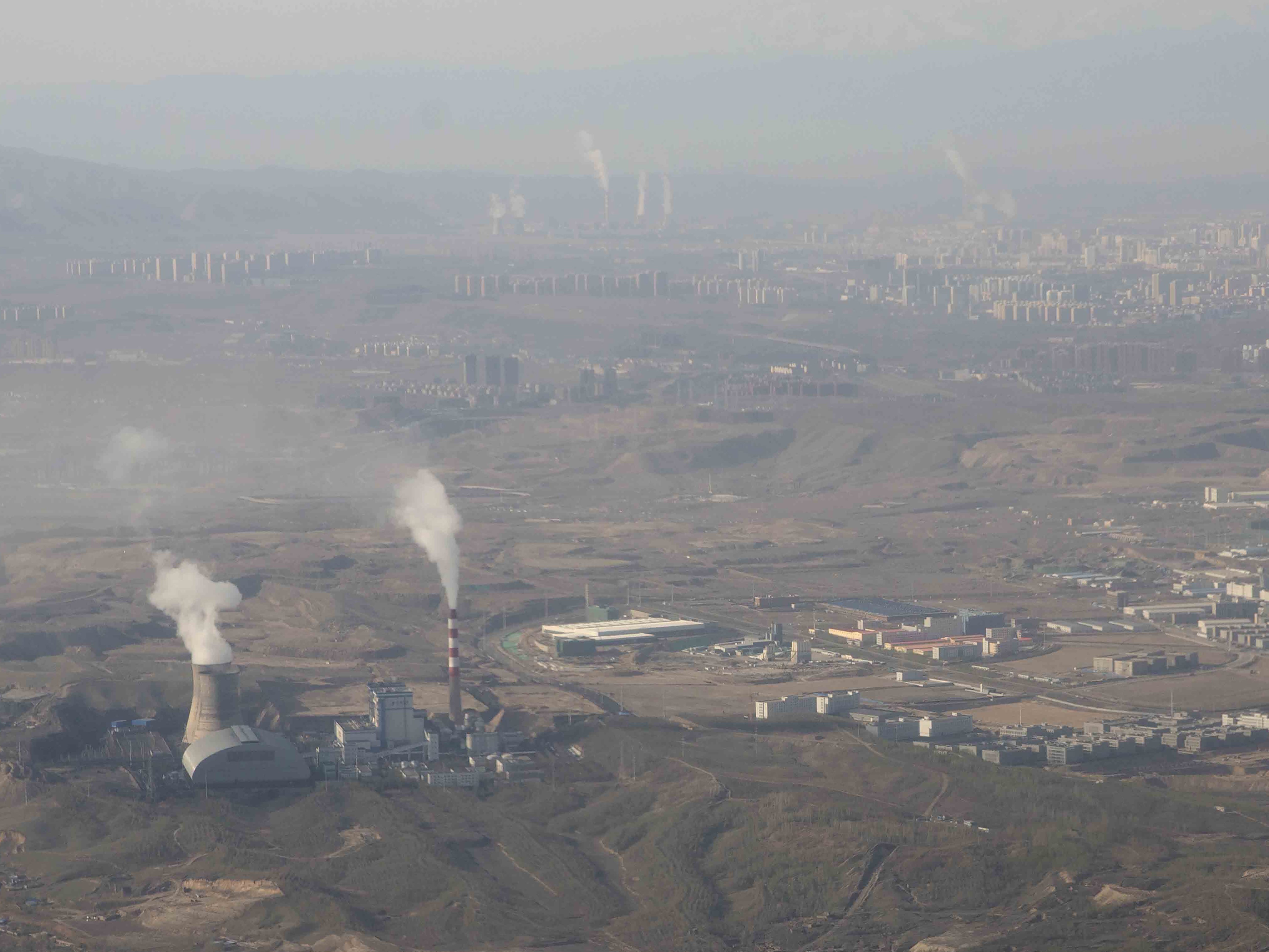caption: Smoke and steam rise from towers at the coal-fired Urumqi Thermal Power Plant as seen from a plane in Urumqi in western China's Xinjiang Uyghur Autonomous Region on April 21, 2021.