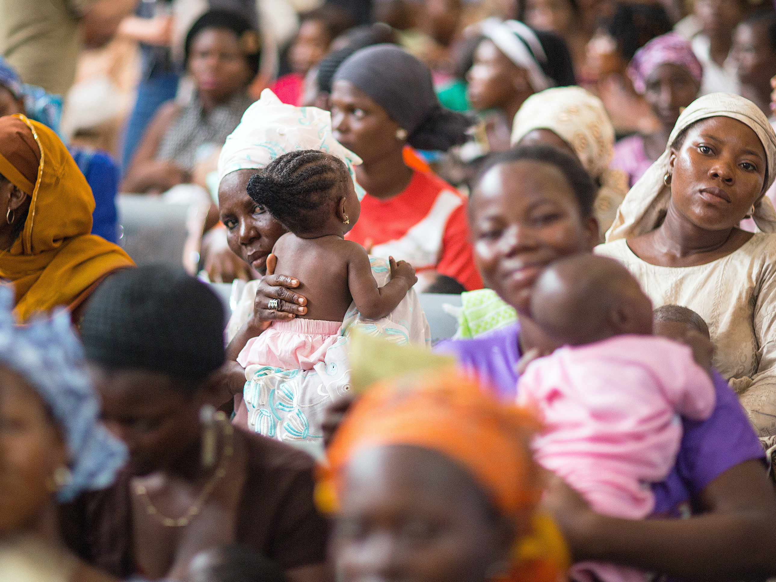 caption: Mothers and their babies in Nigeria wait at a health center that provides vaccinations against polio. Vaccination rates lag in the middle-income country.