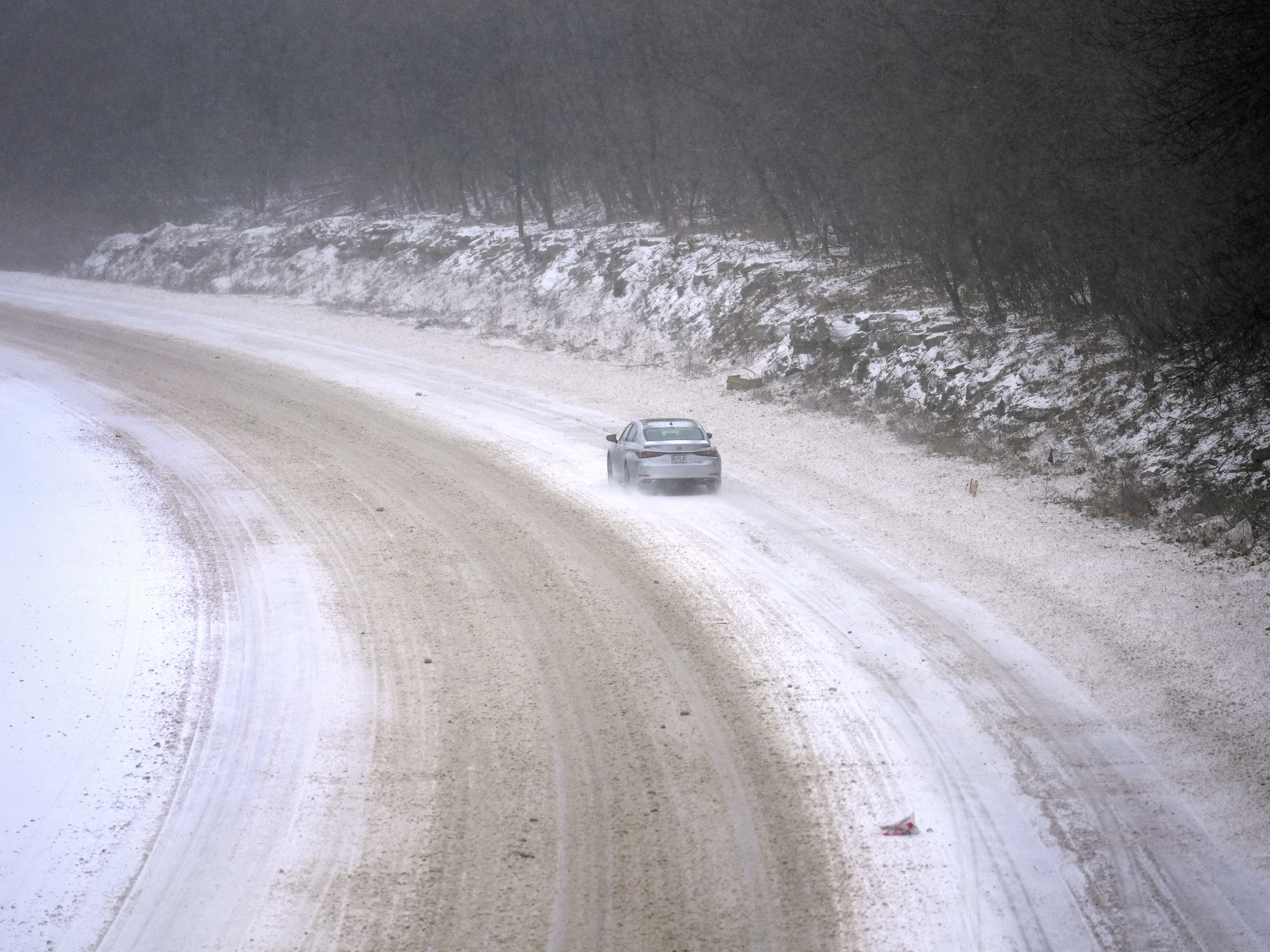 caption: A car slowly navigates a snow-covered interstate on Sunday in St. Louis.