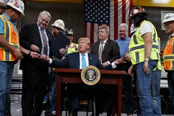 caption: President Trump hands out pens after signing an executive order aimed at making it easier for companies to pursue oil and gas pipeline projects. The president addressed an audience at the International Union of Operating Engineers International Training and Education Center in Texas.