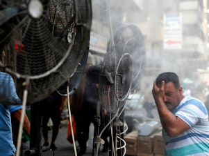 caption: Fans spray air mixed with water vapor to cool down pedestrians on a Baghdad street on June 30, 2021, during a heat wave.