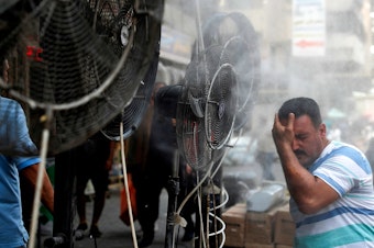 caption: Fans spray air mixed with water vapor to cool down pedestrians on a Baghdad street on June 30, 2021, during a heat wave.