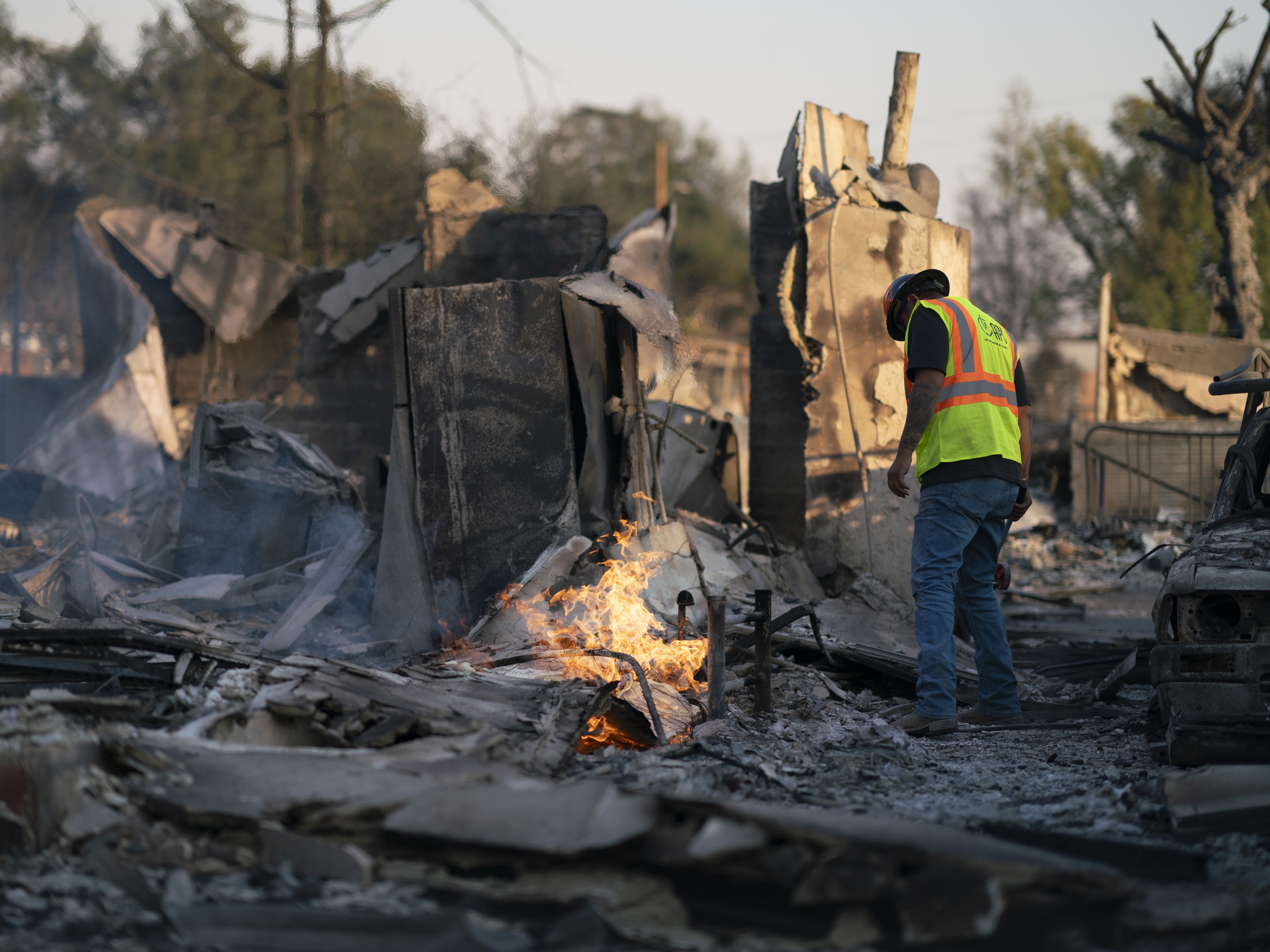 caption: Johnathon Vera with Arizona Pipeline Co. works to extinguish a burning gas line fire in Altadena, Calif., on Jan. 11.
