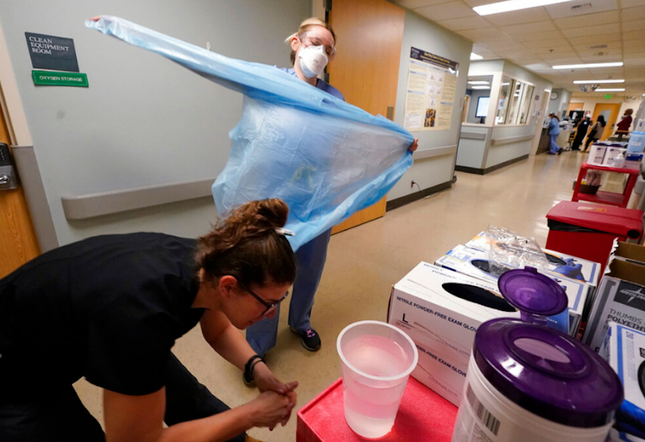 caption: Registered nurse Jessalynn Dest, left, removes protective equipment and washes her hands after leaving a Covid-19 patient's room as speech therapist Sam Gibbs puts on safety clothing while preparing to see a patient in the acute care unit of Harborview Medical Center, Friday, Jan. 14, 2022, in Seattle.