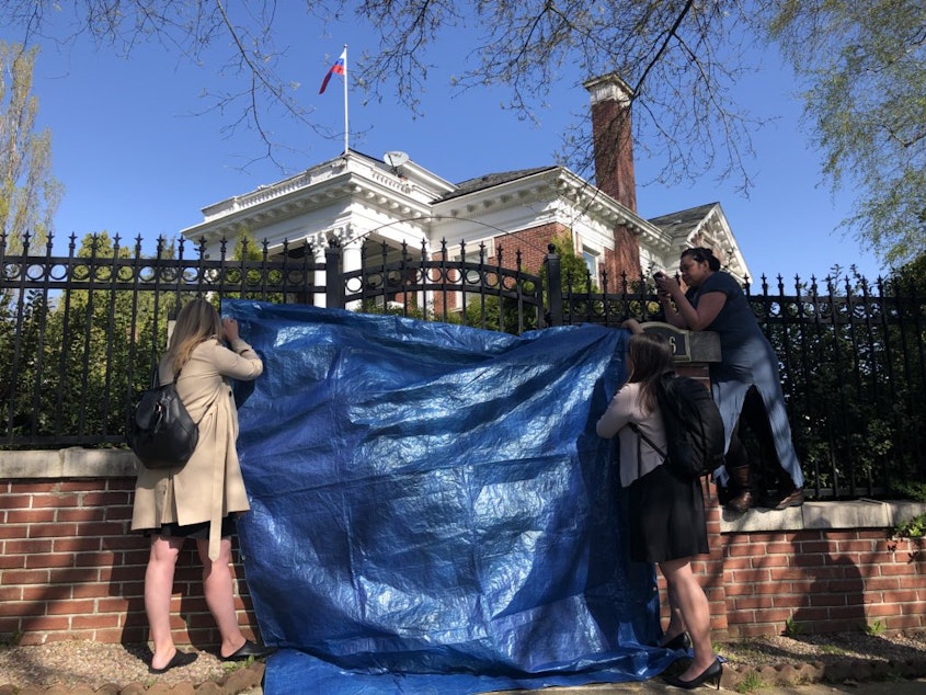 caption: Shielded by an identity-protecting tarp, a Seattle locksmith drills the locks on a Russian-owned consular building.