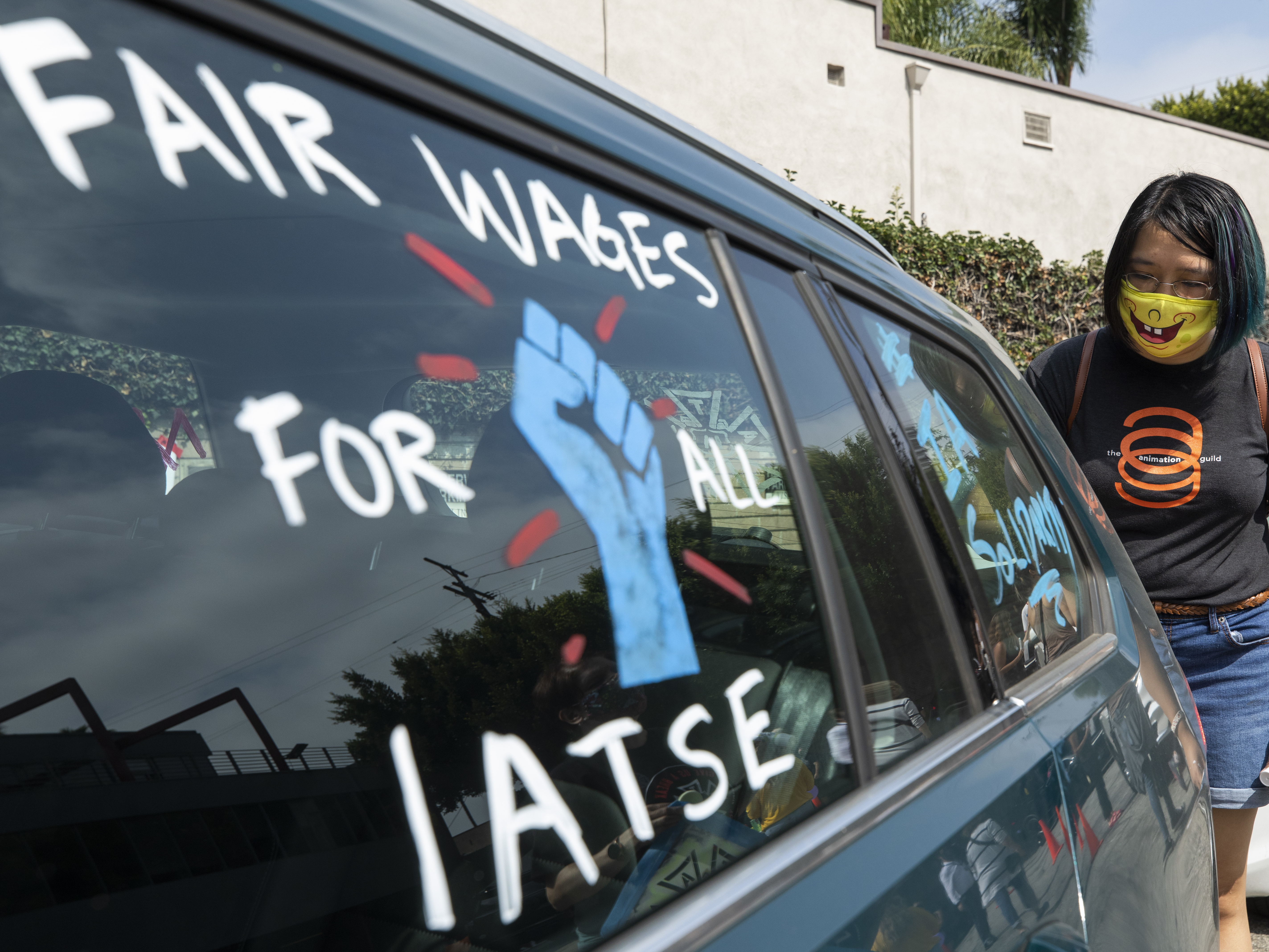 caption: Crystal Kan, a storyboard artist, draws signs on cars of IATSE union members during a rally in Los Angeles in September.