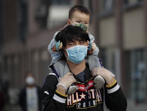 caption: A man carries a toddler on his shoulders on a street in Beijing on Wednesday. While China said it had no new domestic coronavirus cases on Thursday, it reported that dozens more had arrived from abroad.
