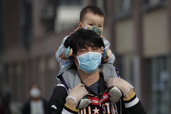 caption: A man carries a toddler on his shoulders on a street in Beijing on Wednesday. While China said it had no new domestic coronavirus cases on Thursday, it reported that dozens more had arrived from abroad.