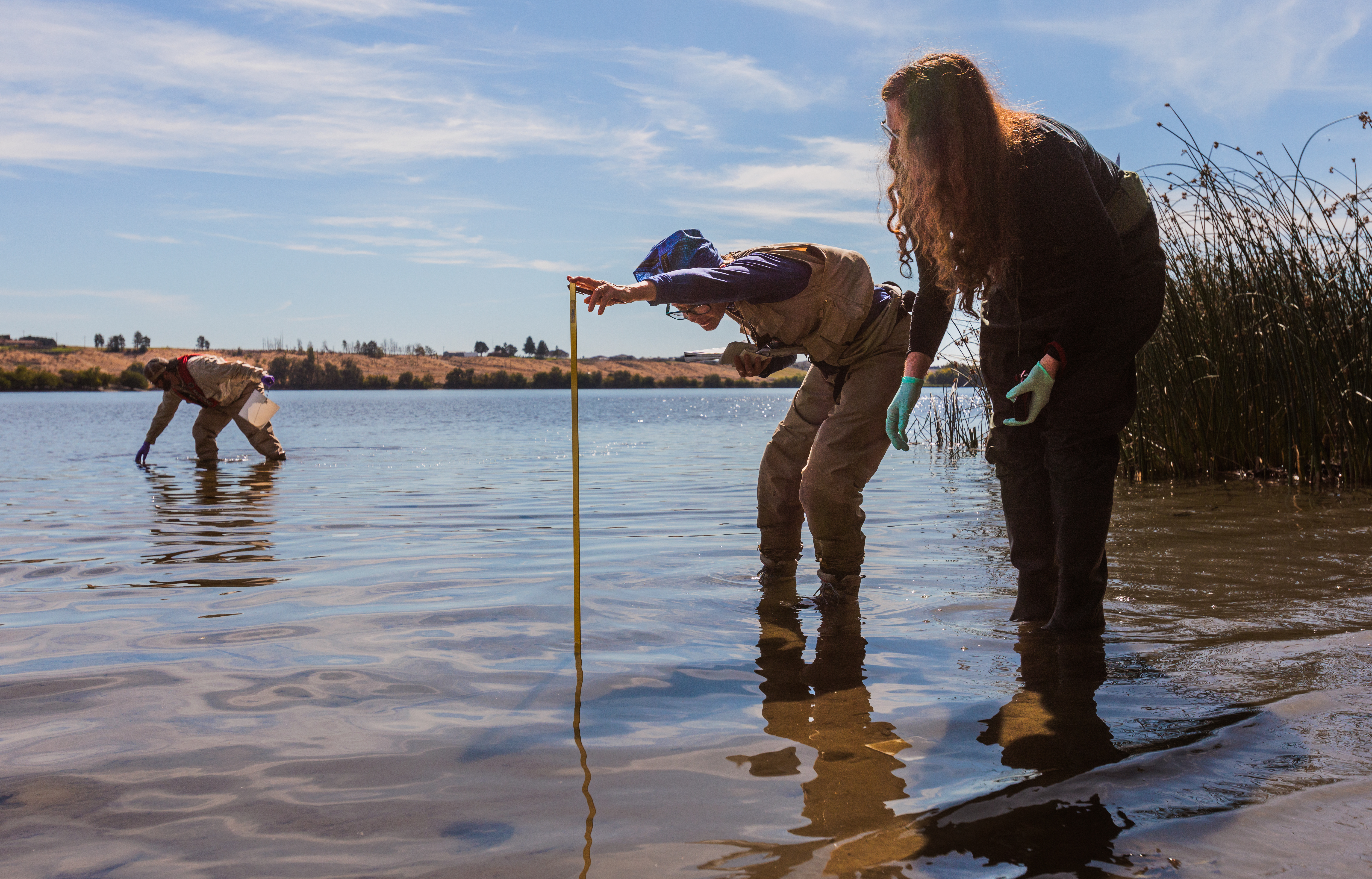caption: U.S. Environmental Protection Agency scientists Rochelle Labiosa (right) and Lil Herger examine the Columbia River for toxic algae as Jason Pappani leans over to reach into the water.