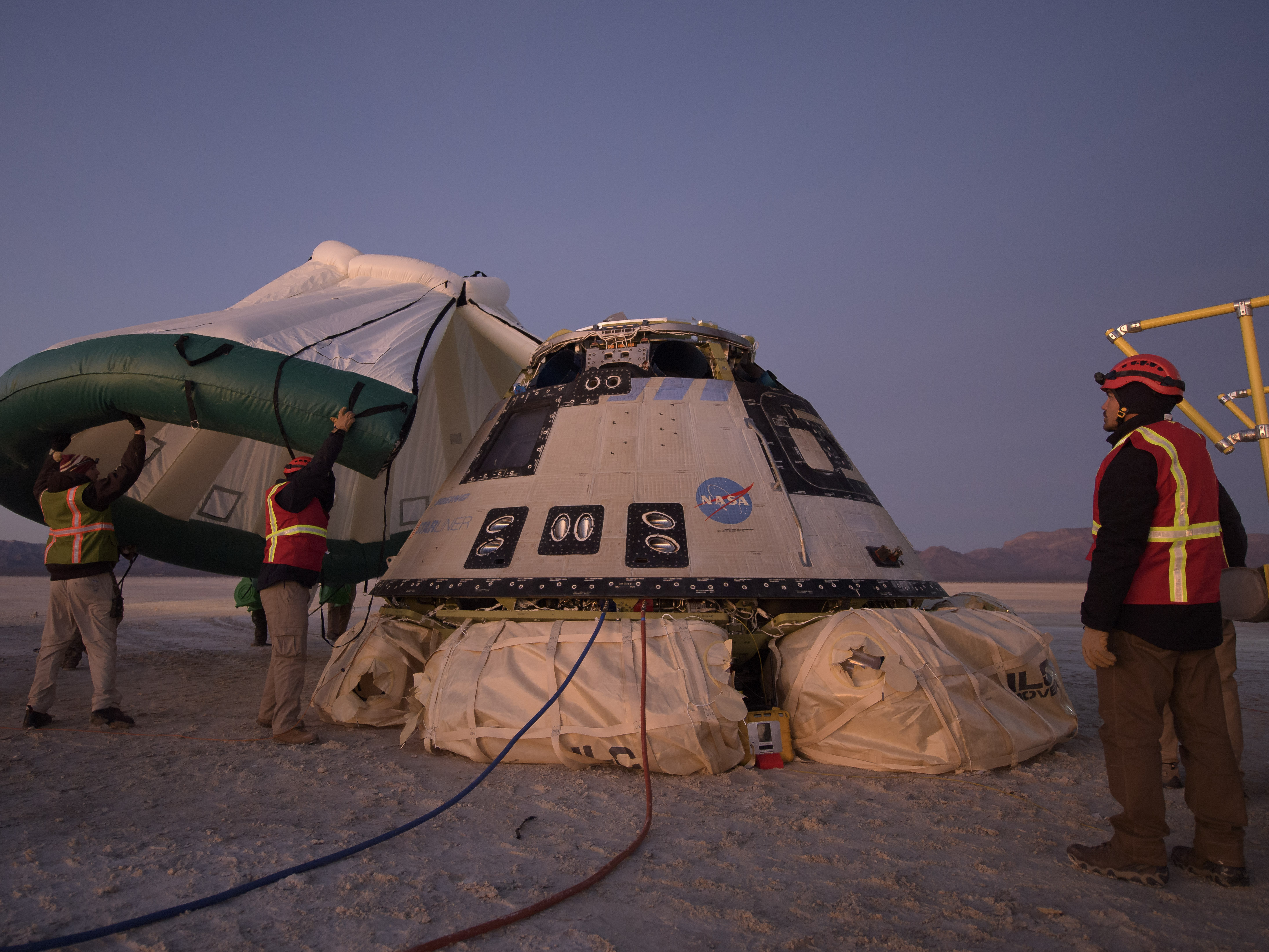 caption: Boeing, NASA, and U.S. Army personnel work around the Boeing Starliner spacecraft shortly after it landed in White Sands, N.M., Sunday.