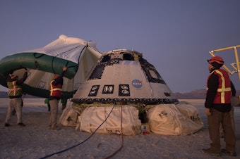 caption: Boeing, NASA, and U.S. Army personnel work around the Boeing Starliner spacecraft shortly after it landed in White Sands, N.M., Sunday.