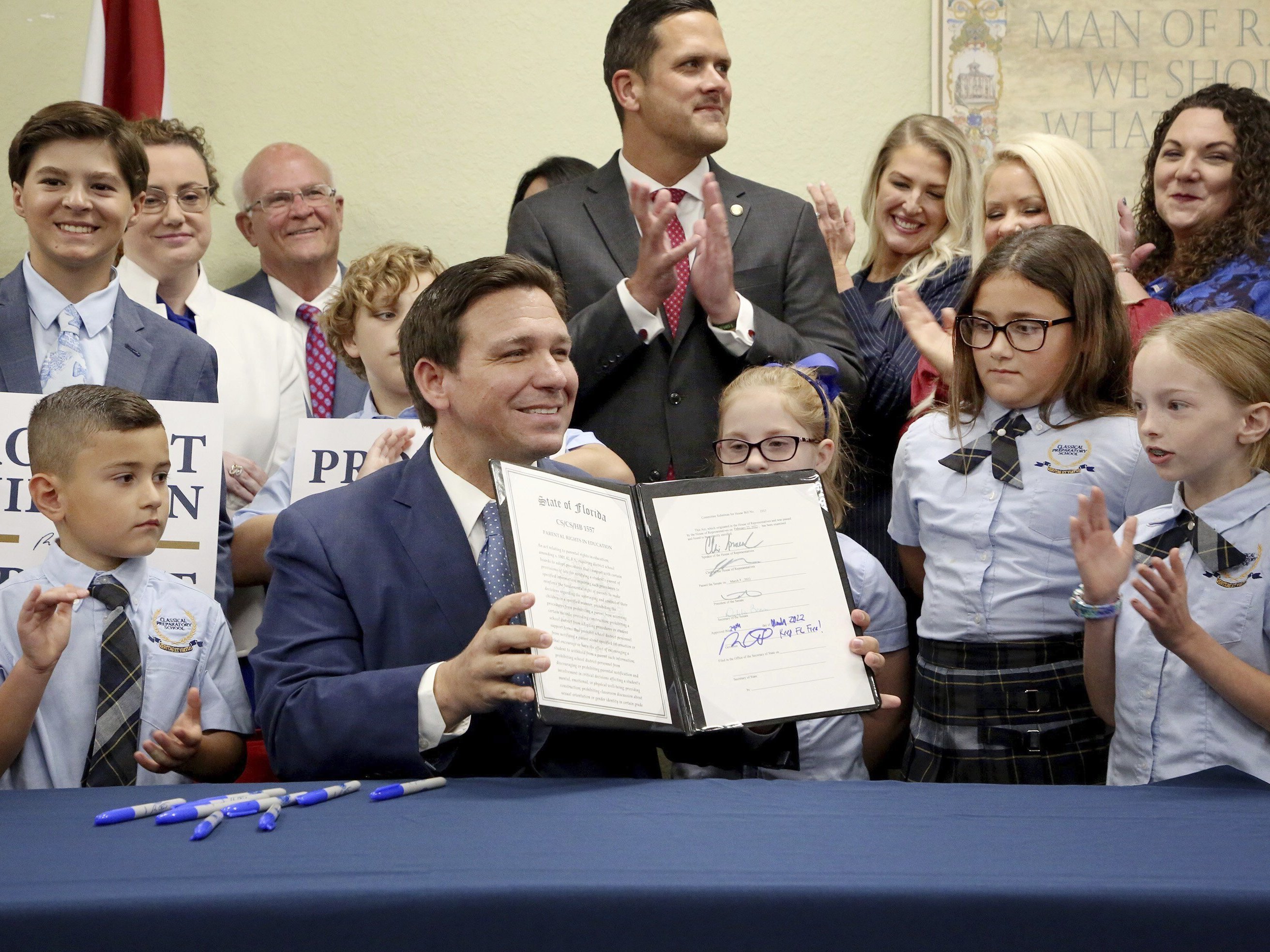 caption: Florida Gov. Ron DeSantis displays the signed Parental Rights in Education, the so-called "Don't Say Gay" bill, flanked by elementary school students during a news conference on Monday at Classical Preparatory school in Shady Hills, Fla.