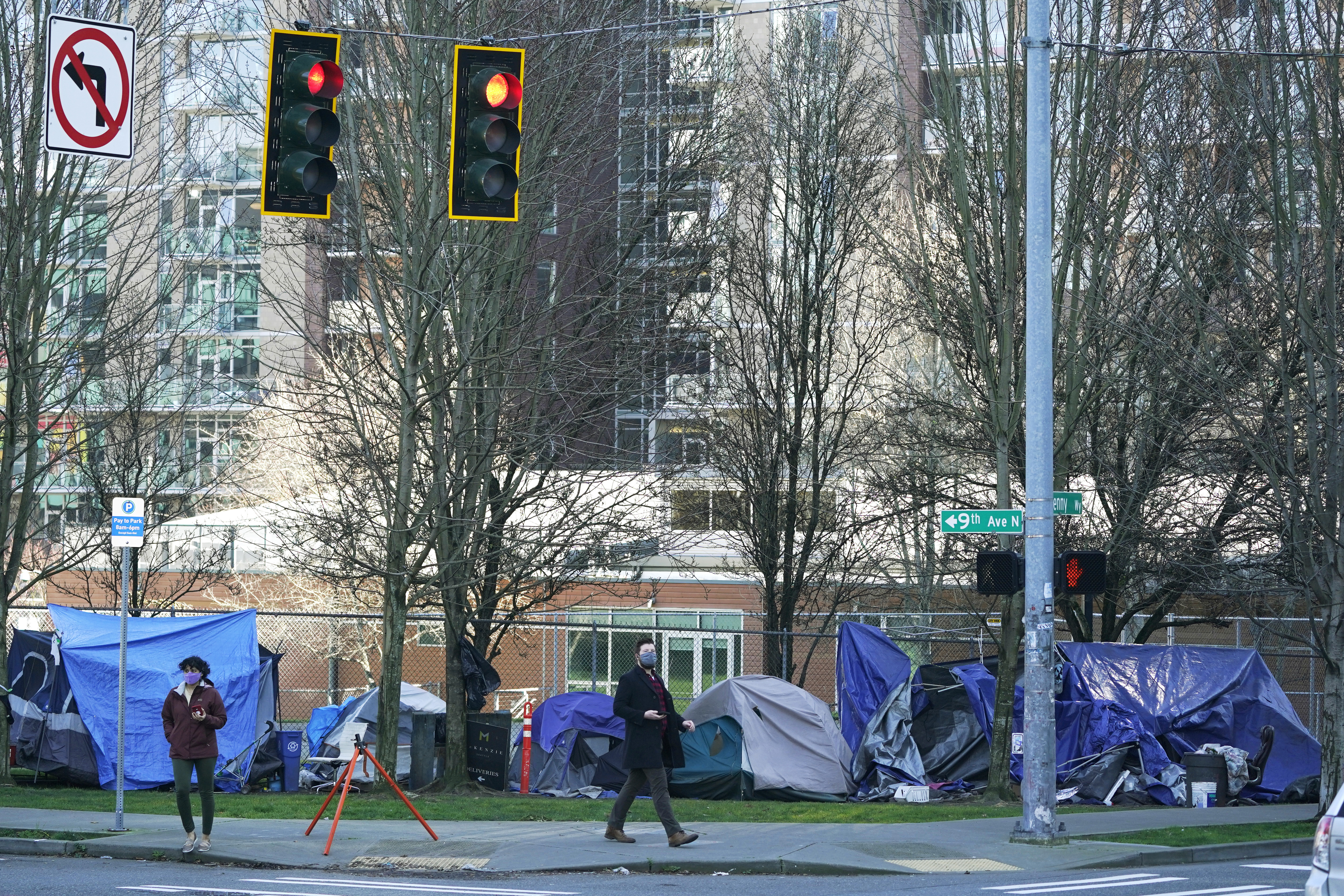 caption: In this March 3, 2021, file photo, with apartment buildings in the background, pedestrians walk past tents used by people lacking housing at Denny Park near the Space Needle in Seattle. A Washington state judge on Friday, Aug. 27, 2021, struck a Seattle measure on homelessness from the November ballot even as the city remains mired in a long-term humanitarian crisis.