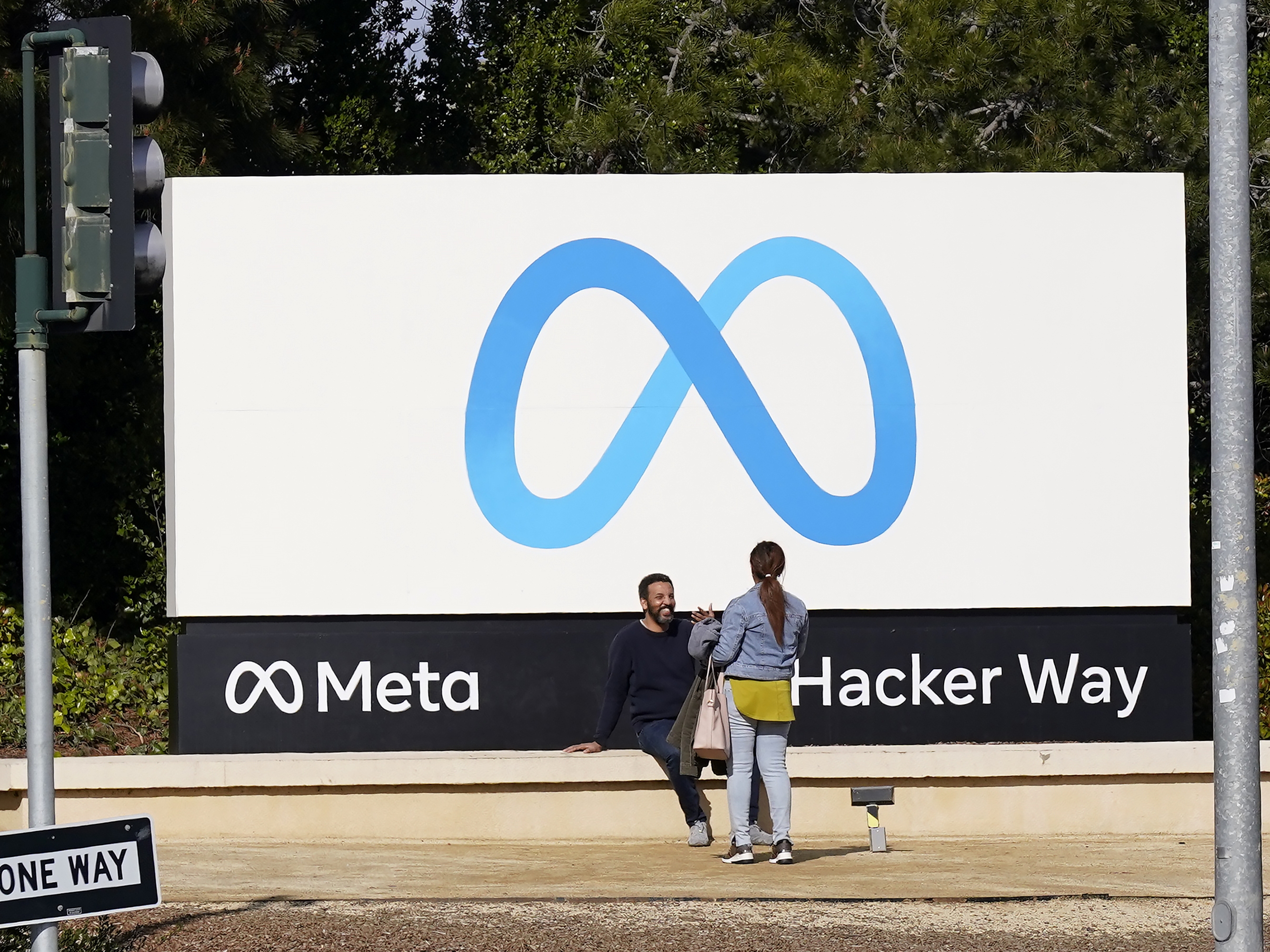 caption: People talk near a Meta sign outside of the company's headquarters in Menlo Park, Calif.