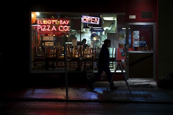 caption: A pedestrian walks in front of the Elliott Bay Pizza Co. & Flame Burger on Monday, November 16, 2020, along Queen Anne Avenue North in Seattle. New statewide restrictions, including a ban on indoor dining beginning Wednesday, were announced by Gov. Jay Inslee on Sunday to curb the rapid spread of Covid-19. 