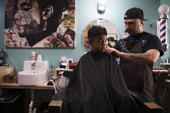 caption: Jayden Valencia, 6, has his hair cut by Chuck Hyte, right, at Uptown Barbershop on 4th St., on Thursday, June 8, 2017, in Bremerton, Washington. 
