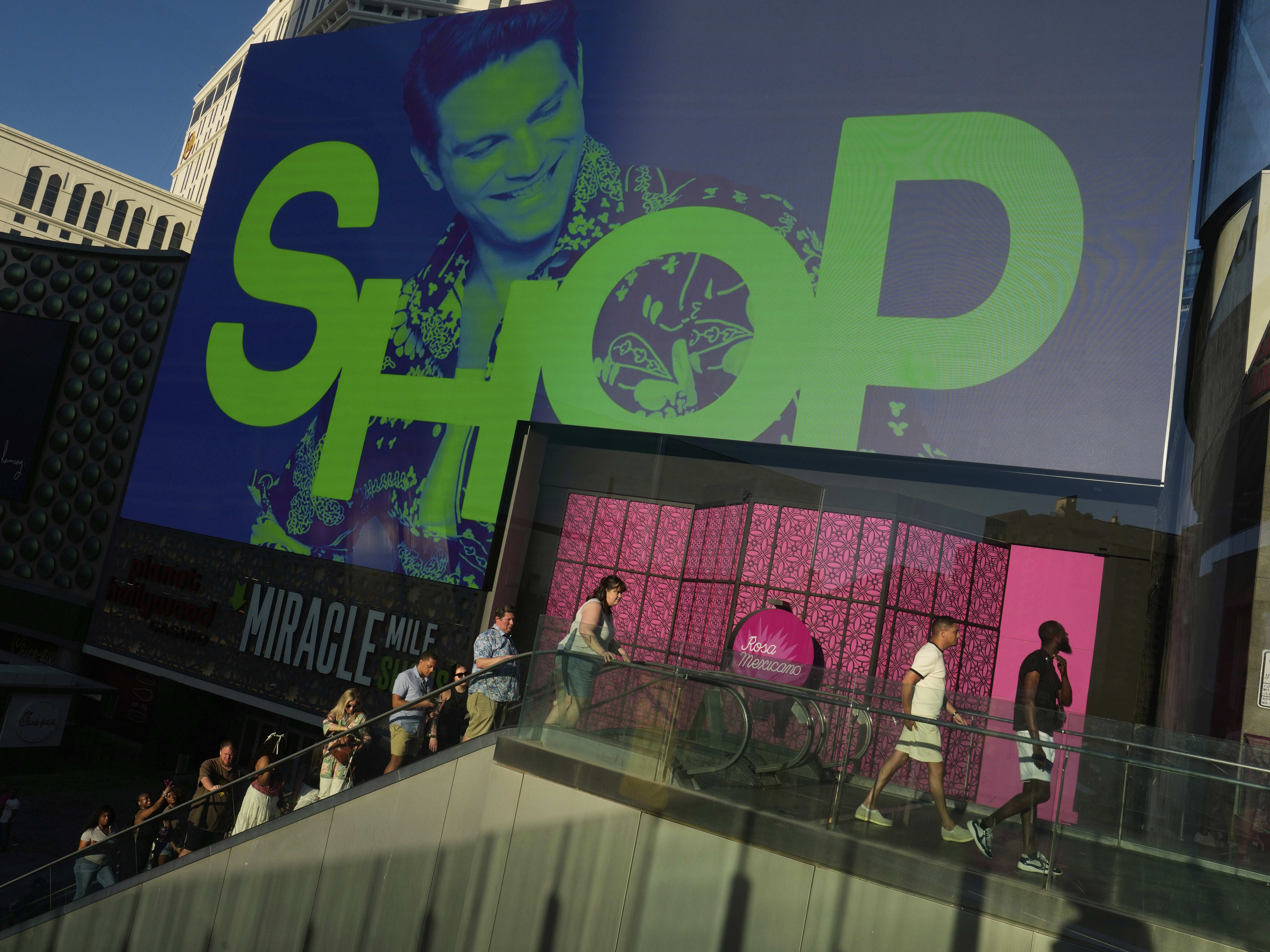 caption: People walk by a shopping mall along the Las Vegas Strip on April 8, 2025.
